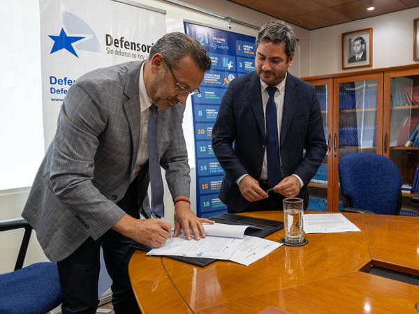 El Defensor Nacional, Carlos Mora Jano, suscribiendo el acuerdo junto al director de la carrera de derecho de la UAH, Alexander Docmac.